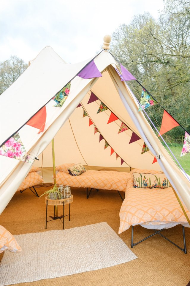 Interior of 5m bell tent at hen camp, showing beds with colourful duvets, and colourful bunting hung from the roof of the tent.