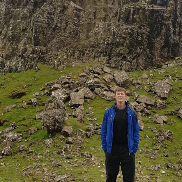 Jamie stood infront of a mountain wearing a blue coat