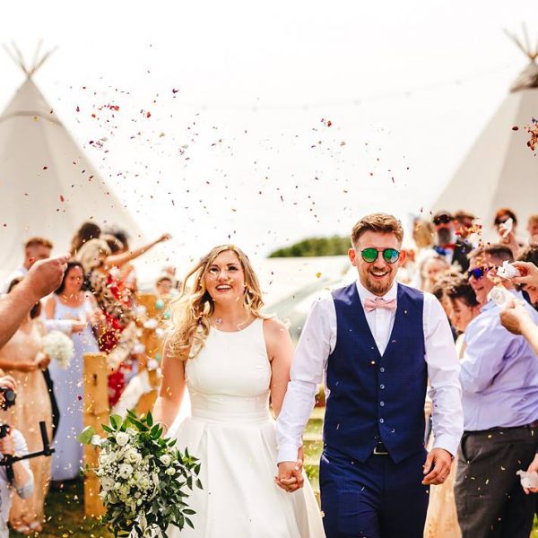 Abi and Greg walking through confetti. Outdoor wedding inspiration. Bell tent hire West Sussex