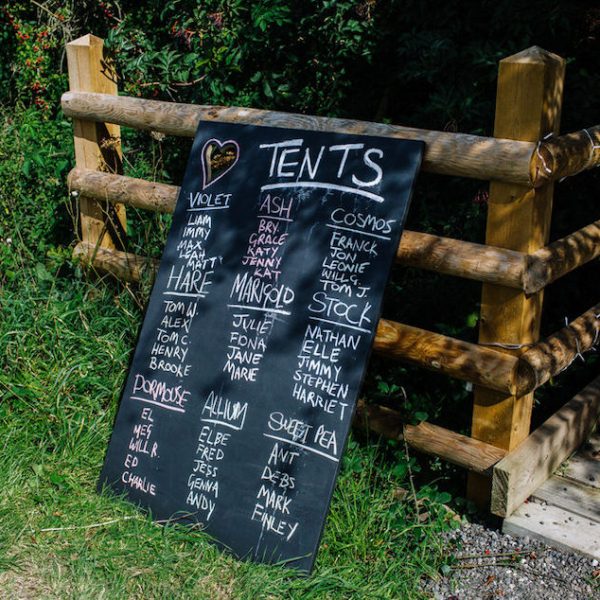 Black board with tent names written on for guests. Bell tent hire, The Secret Barn, West Sussex. Outdoor wedding inspiration.